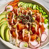A close-up shot of a homemade poke bowl, showing marinated tuna atop fluffy rice and vibrant toppings.