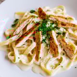 Golden, spicy Cajun chicken slices resting on silky Alfredo fettuccine, garnished with red pepper flakes and herbs.