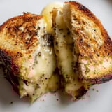 Slices of crispy Truffle Grilled Cheese with Gruyère and truffle oil, served on a slate board, ready to be dipped into tomato soup.