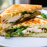 Close-up of a Chicken Pesto Panini showing juicy grilled chicken, vibrant green basil pesto, and fresh tomato slices.