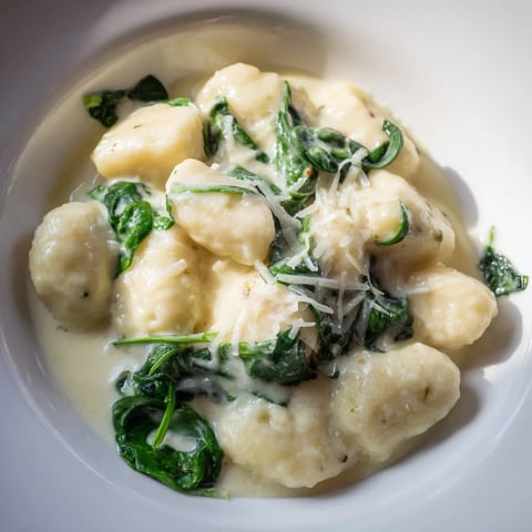 Soft, steaming Creamy Garlic Gnocchi in a velvety white sauce, garnished with fresh spinach and a generous dusting of Parmesan.