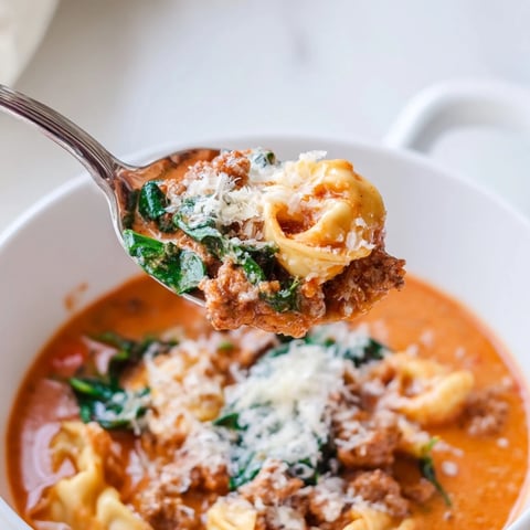 Creamy Tuscan Tortellini Soup with Italian sausage and fresh spinach, served steaming in a rustic bowl.