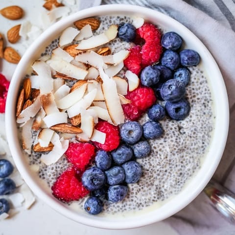 A close-up of creamy Poppy Seed Chia Pudding with a spoon resting beside fresh raspberries.