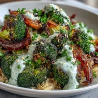 Roasted Broccoli Bowl topped with creamy tahini sauce, sliced avocado, and fresh parsley served over fluffy quinoa grains.