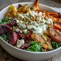 Golden roasted root vegetables like carrots and sweet potatoes rest on a bed of massaged kale in a Winter Root Vegetable Bowl. 